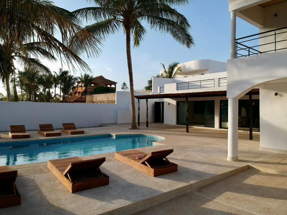 Terrasse de piscine avec transats en bois devant la villa blanche